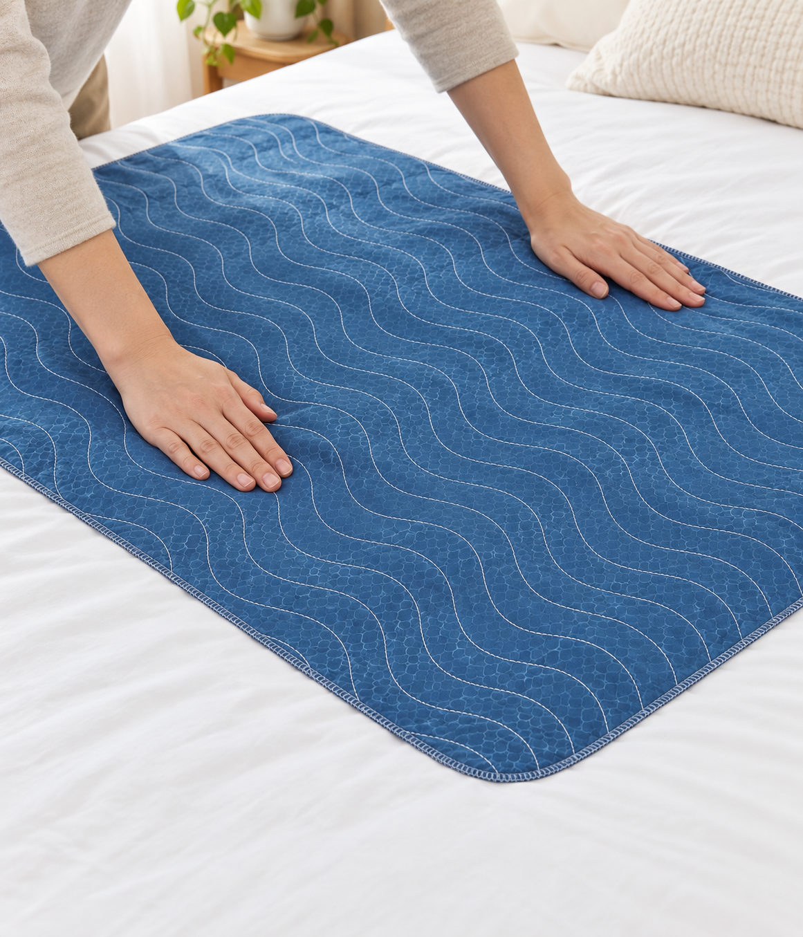Hands laying a washable care pad flat across a made bed